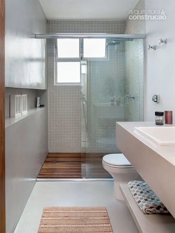 Banheiro branco com parede de cimento queimado e box com piso de deck