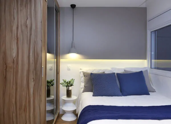 Quarto pequeno com decoração moderna e simples. Pendente na lateral da cama e cama no canto.